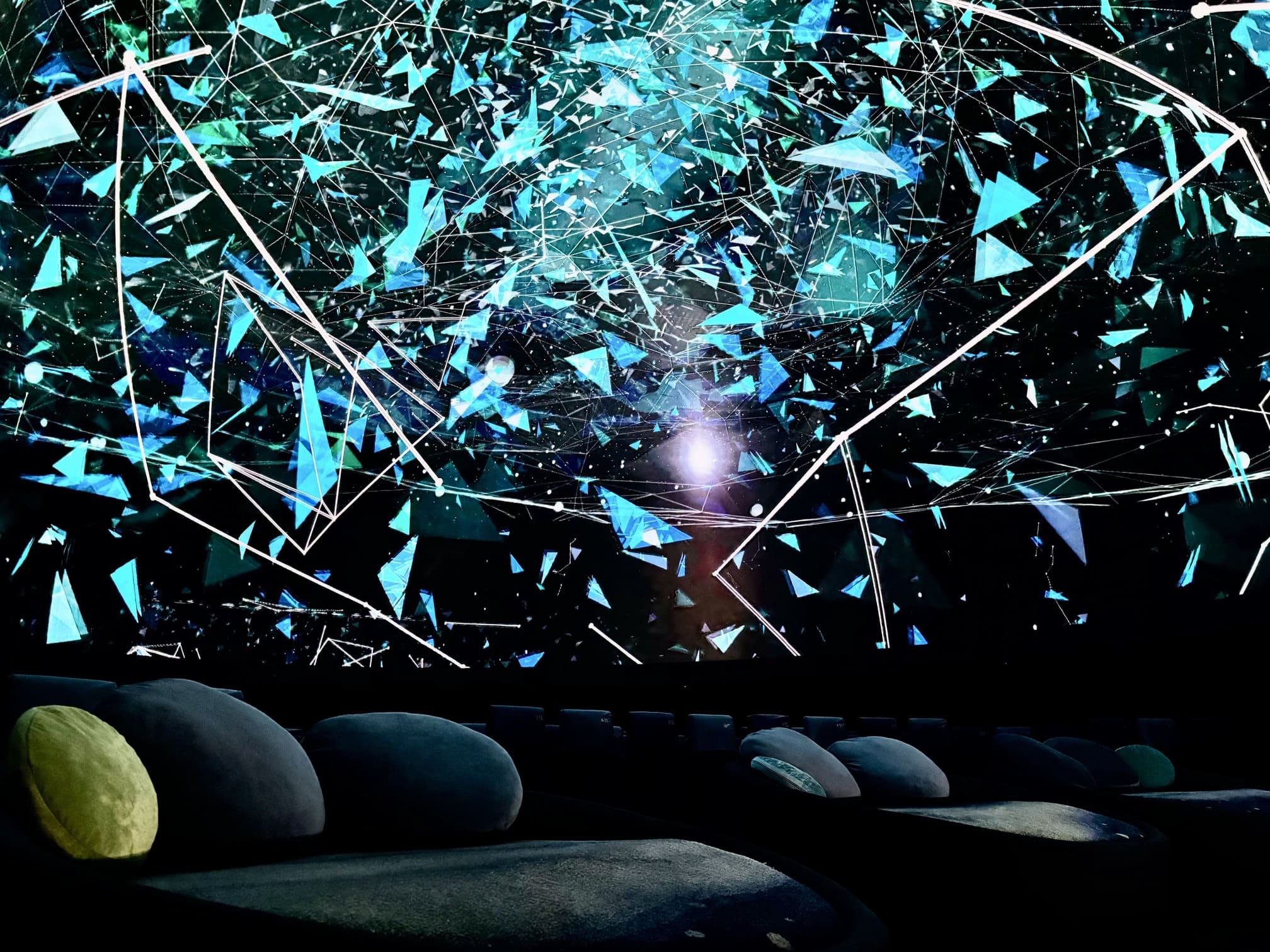 Dark theater interior featuring an abstract digital installation of blue triangles and white interconnected lines overhead.