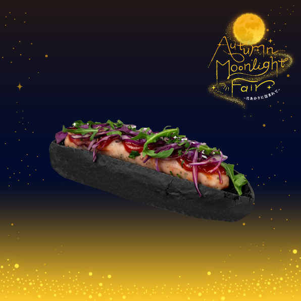 A hot dog with a black bun topped with greens and red onions floats in a starry night backdrop with a gold Autumn Moonlight Fair logo in the corner.