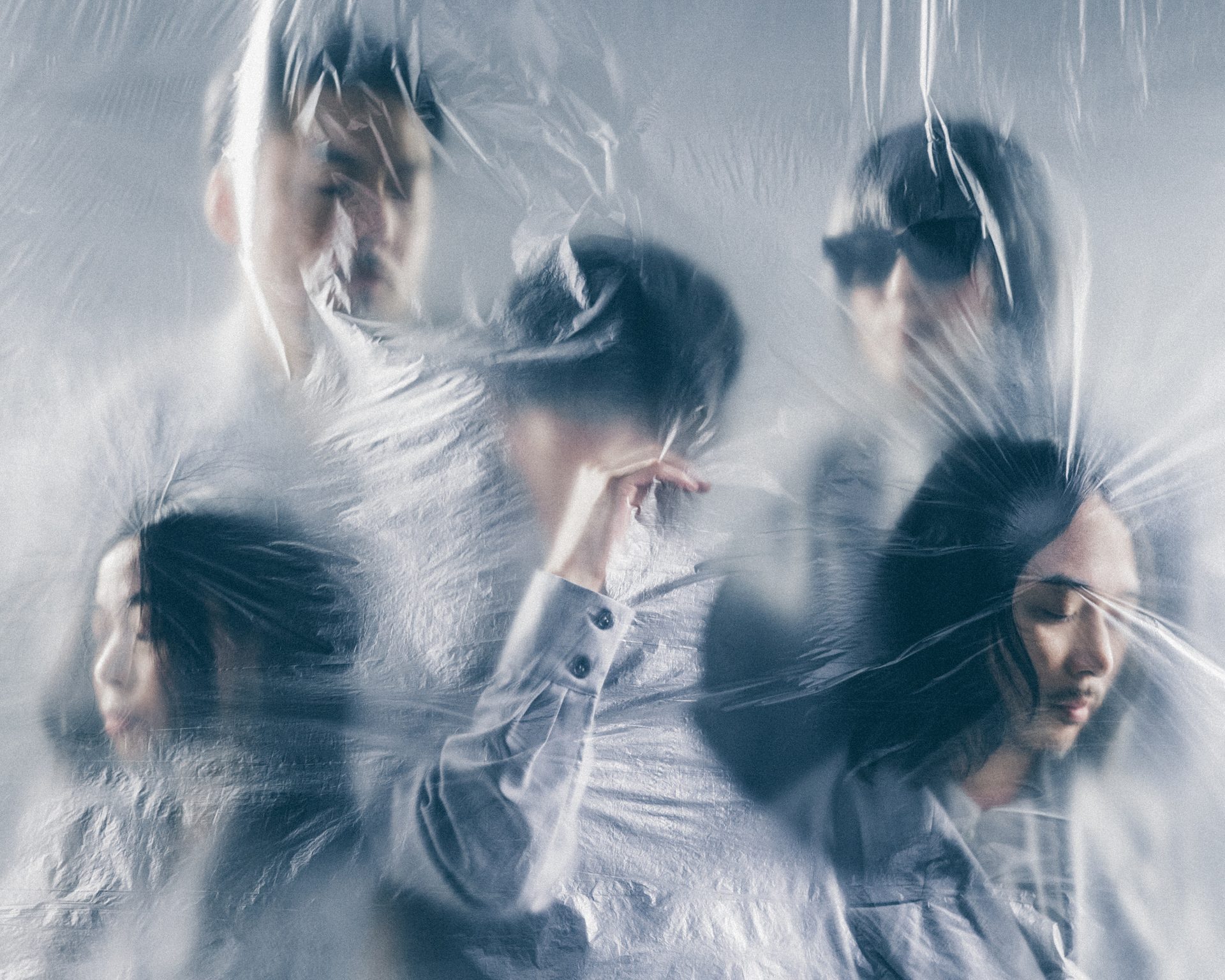 People seen through a wrinkled plastic sheet, creating a hazy, dreamlike group portrait in cool blue tones.